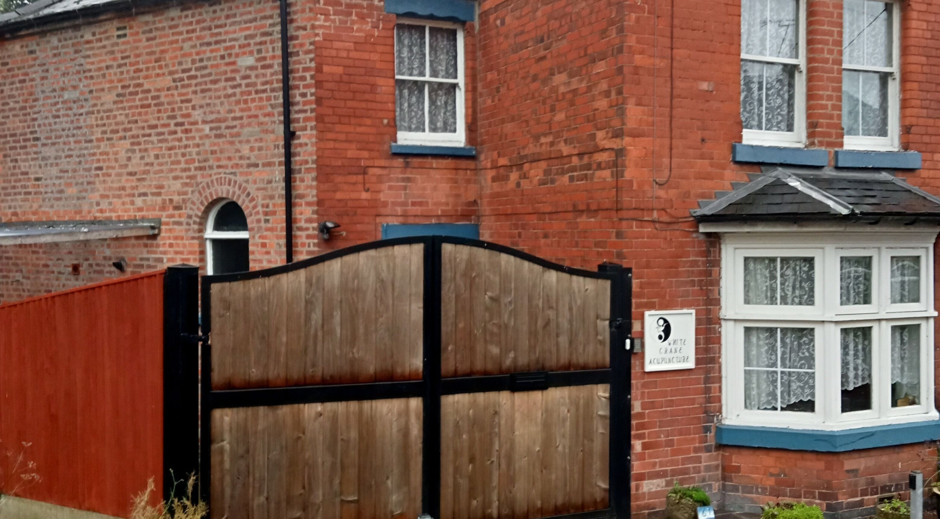 Front entrance of White Crane Acupuncture, Mansfield, GB, showcasing its charming redbrick exterior and gate.