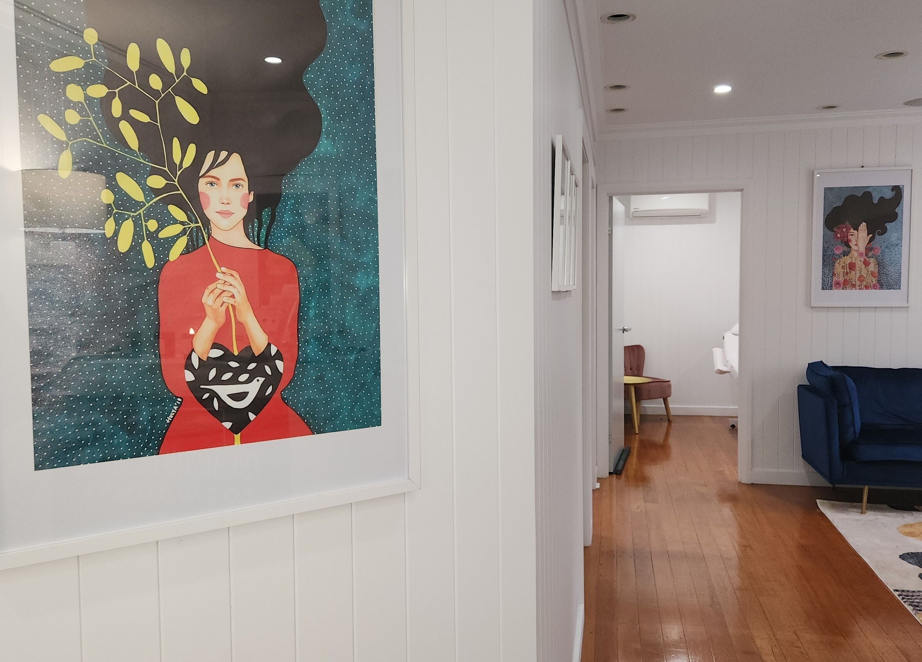 Interior of The Aesthetic Studio Toowoomba, featuring modern art on white walls and a cozy blue sofa.