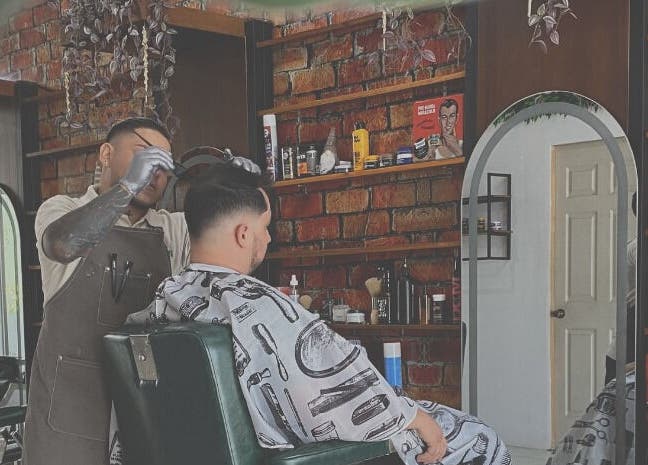 Barbero atendiendo cliente en Plaza Natura Garten Barberclub, Managua, Managua, NI. Ambiente moderno con ladrillos.