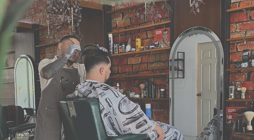 Barbero atendiendo cliente en Plaza Natura Garten Barberclub, Managua, Managua, NI. Ambiente moderno con ladrillos.