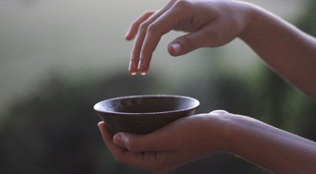 Hand holding bowl with water drop at Nurture, Byron Bay, New South Wales, AU, promoting relaxation.
