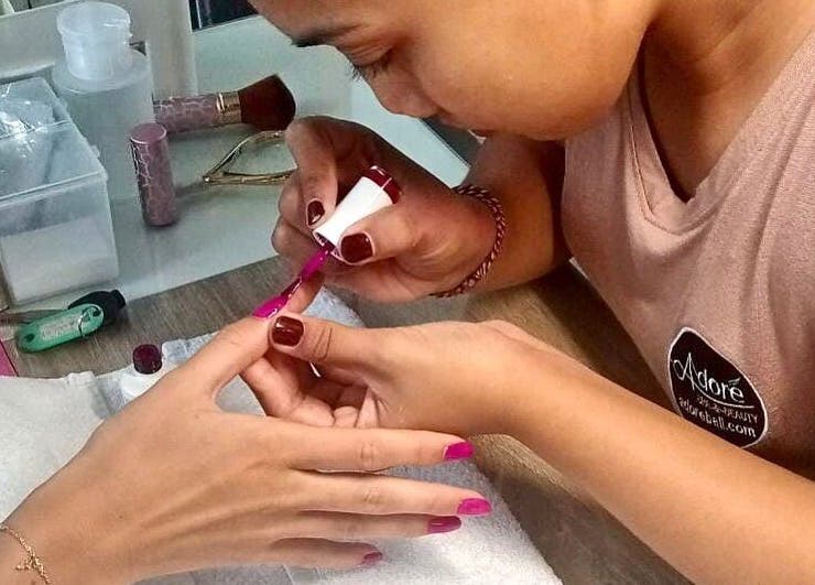 Nail artist at Adore Nails & Massage in Bali, Bali, ID applying vibrant polish to client's nails.