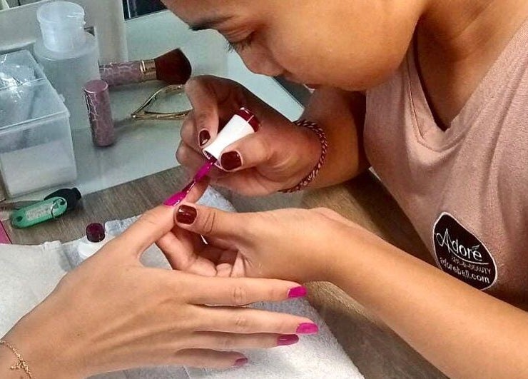 Nail artist at Adore Nails & Massage in Bali, Bali, ID applying vibrant polish to client's nails.
