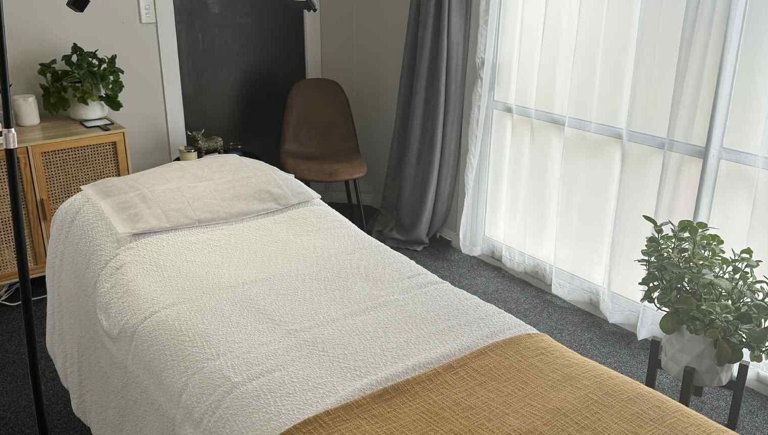 Tranquil treatment room at Haven Beauty, Taupō, Waikato, NZ, featuring a cozy bed and lush plants by window.