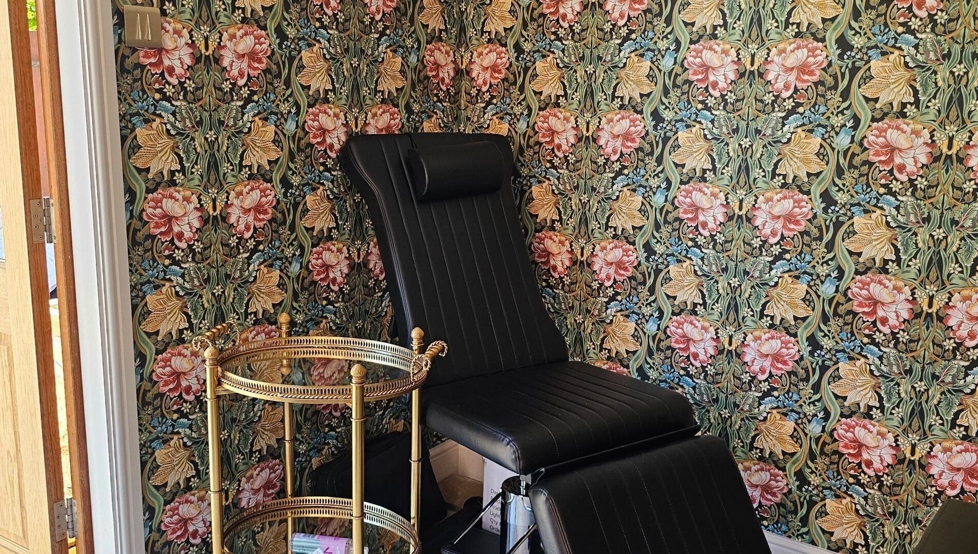 Elegant black chair in Monique's Hair Extension Boutique, Great Finborough, England, with floral wallpaper.