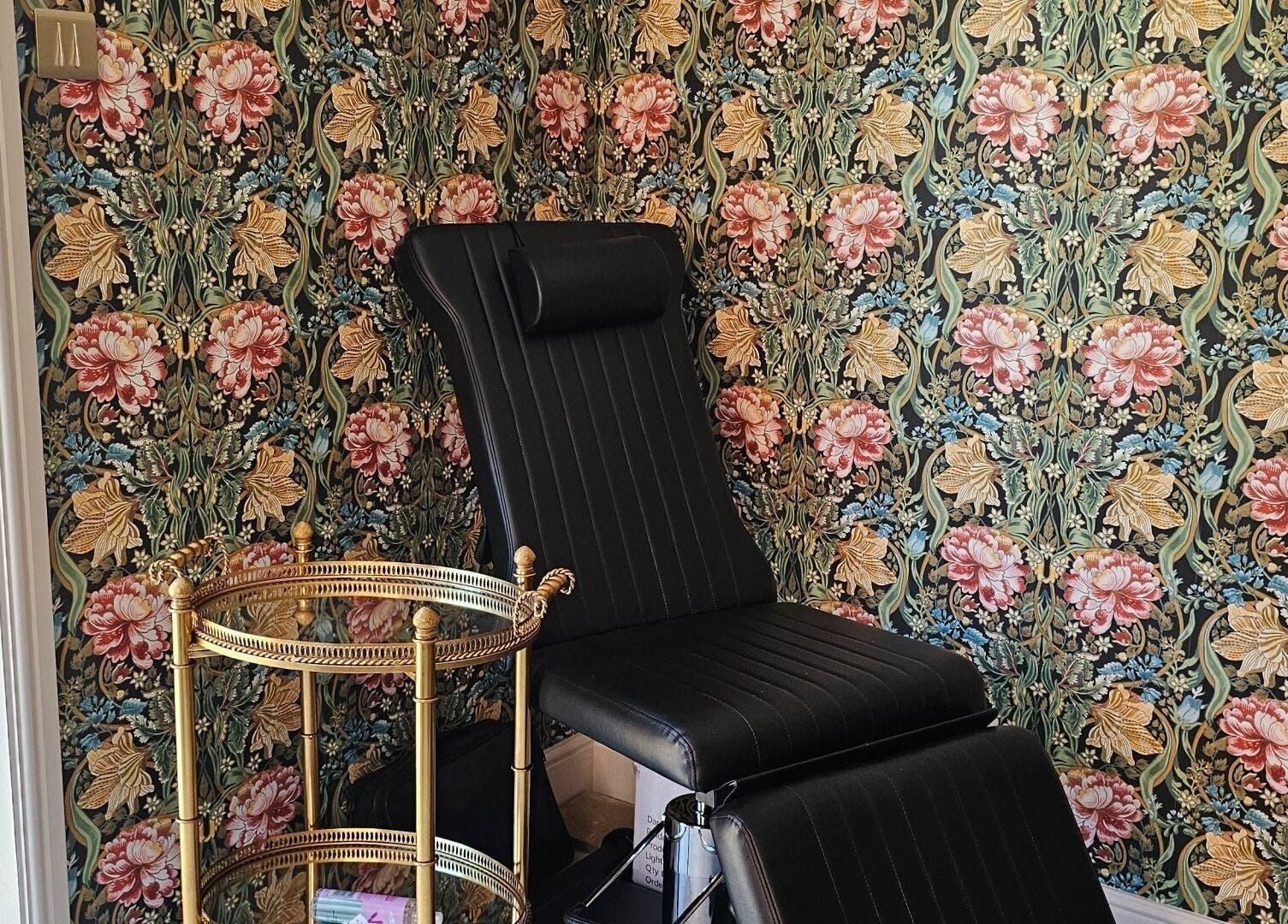 Elegant black chair in Monique's Hair Extension Boutique, Great Finborough, England, with floral wallpaper.