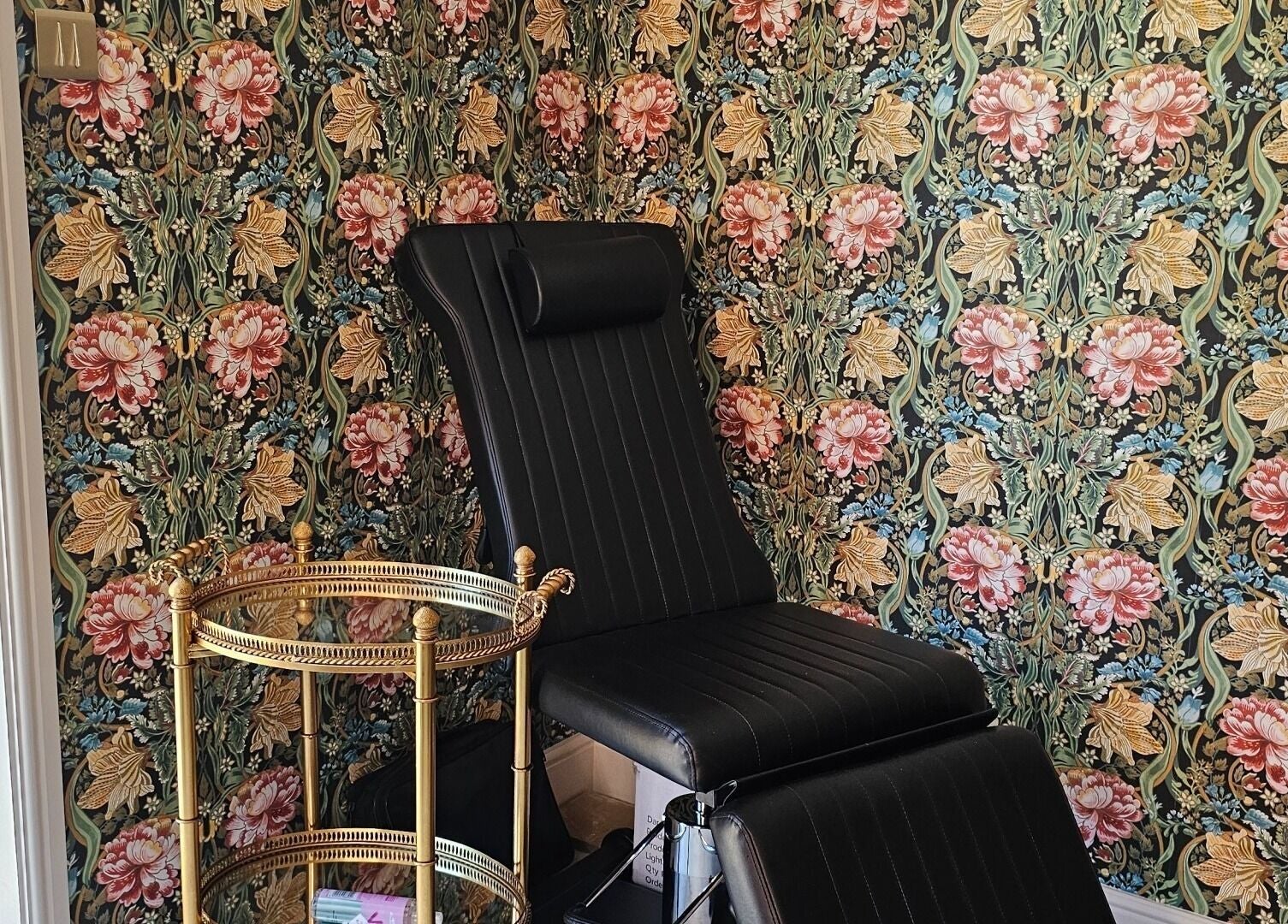 Elegant black chair in Monique's Hair Extension Boutique, Great Finborough, England, with floral wallpaper.