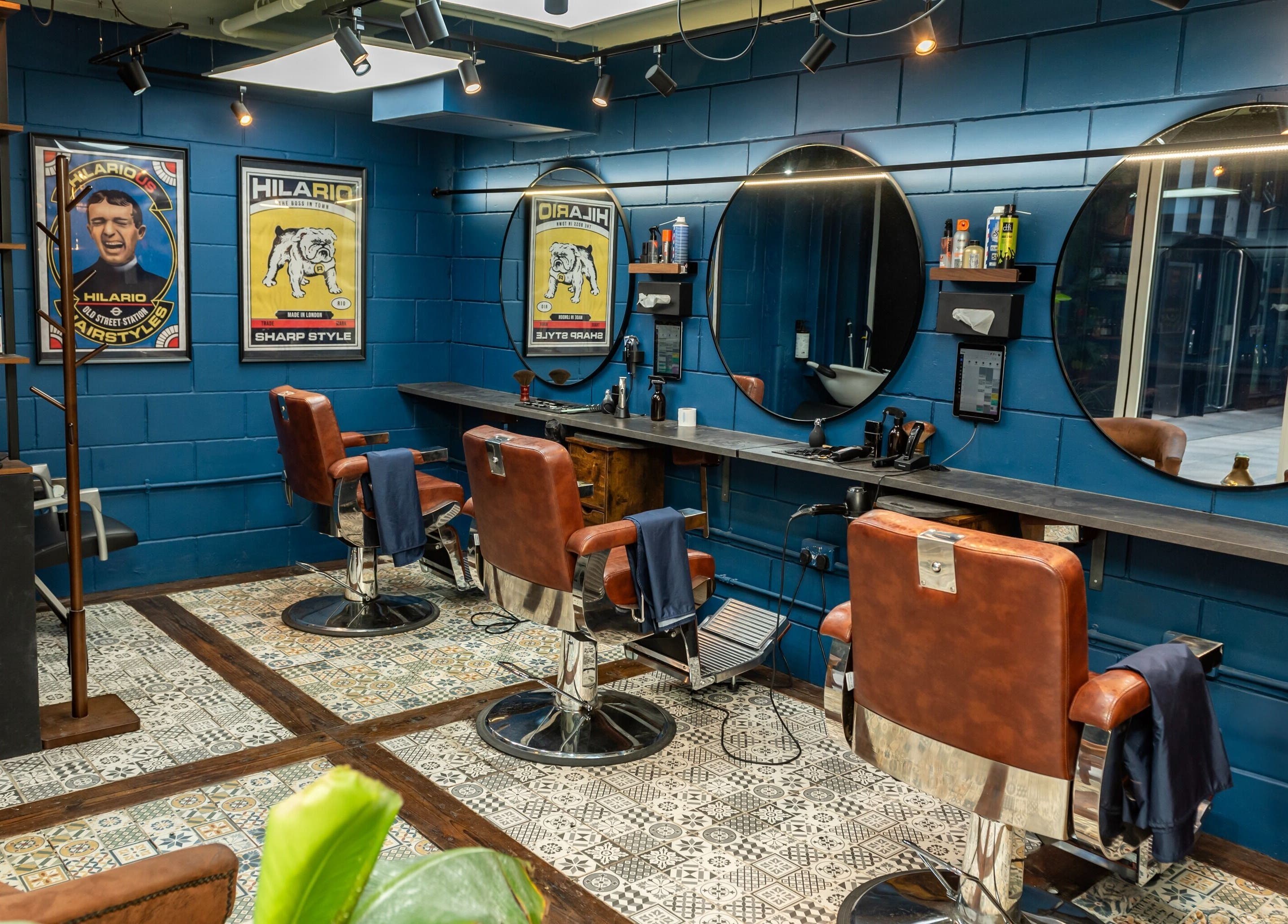 Vintage-style barber chairs at Hilario, London, England, GB, with blue walls and circular mirrors, creating a stylish ambiance.