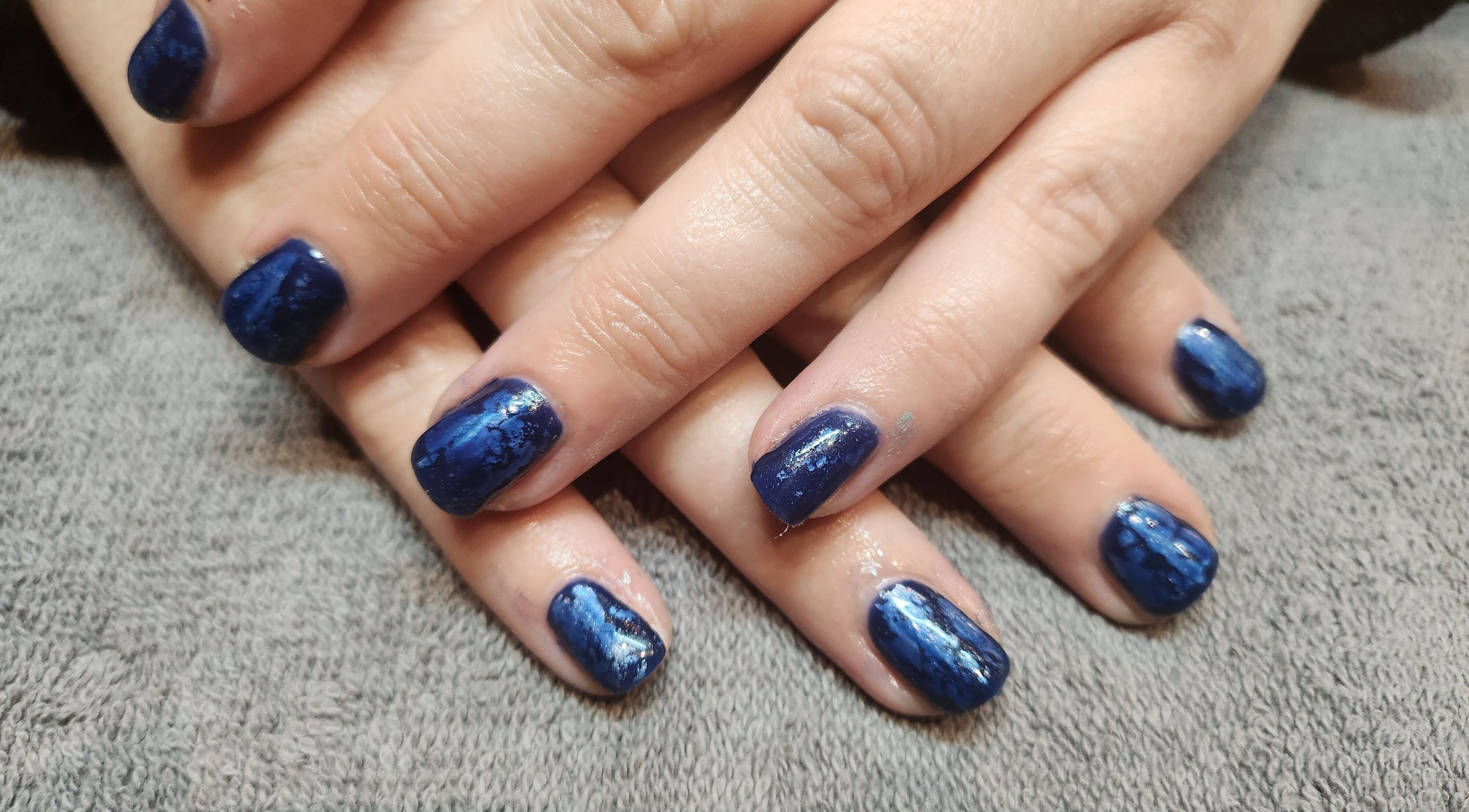 Elegant blue nail art at At One, Kingswinford, England, GB on a plush gray surface.