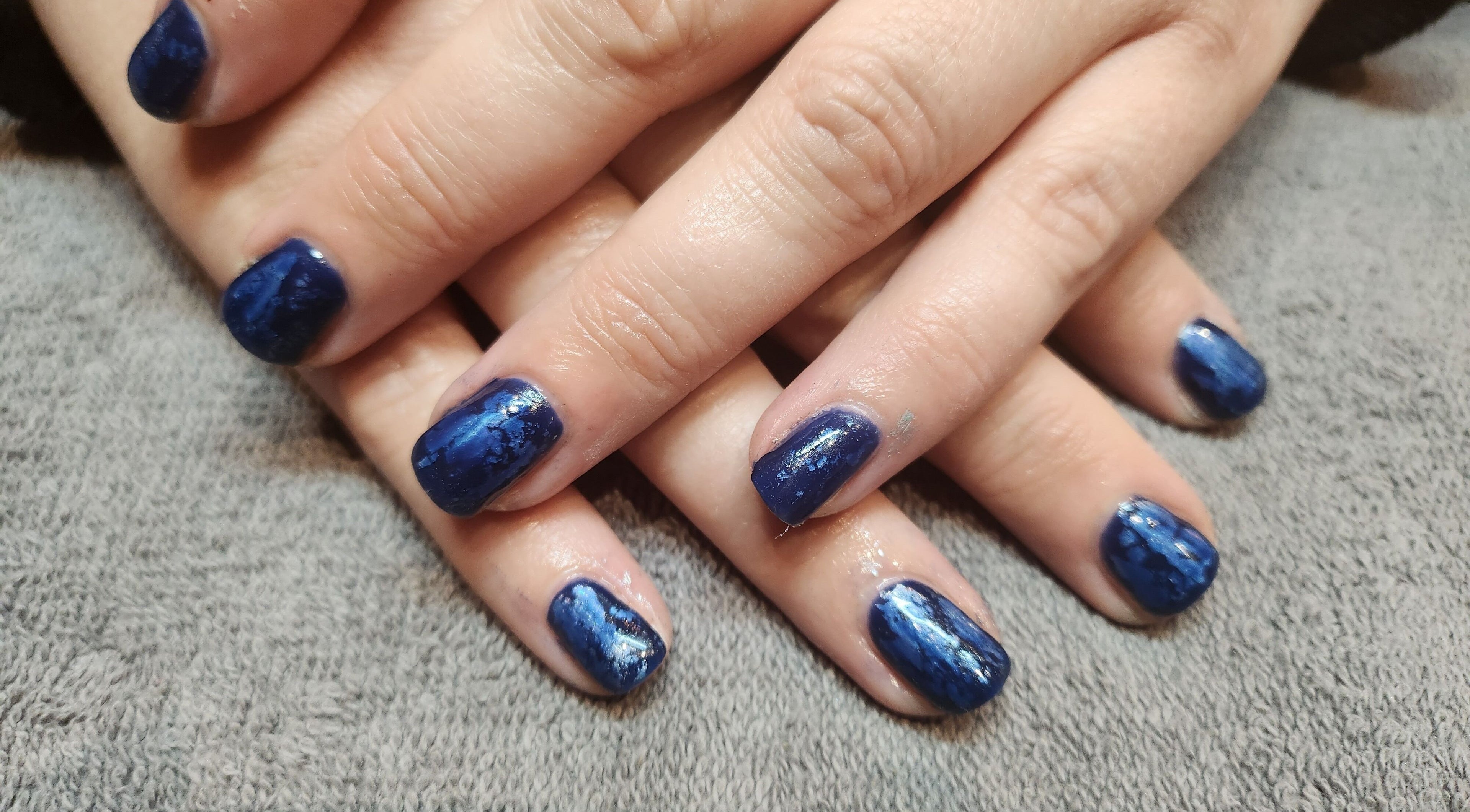 Elegant blue nail art at At One, Kingswinford, England, GB on a plush gray surface.