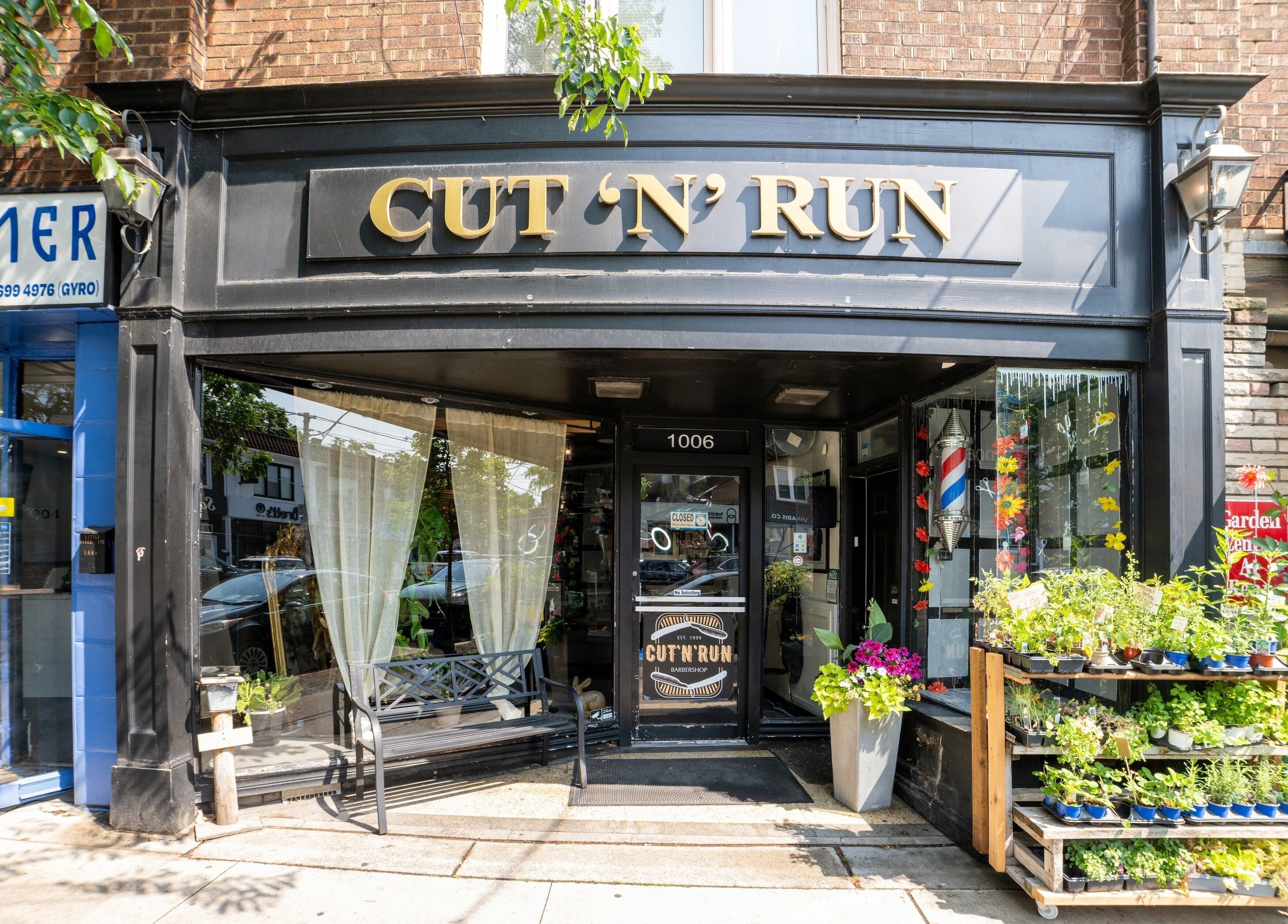 Front view of Cut N Run Barbershop in Toronto, Ontario, CA, with its stylish black facade and lush greenery.