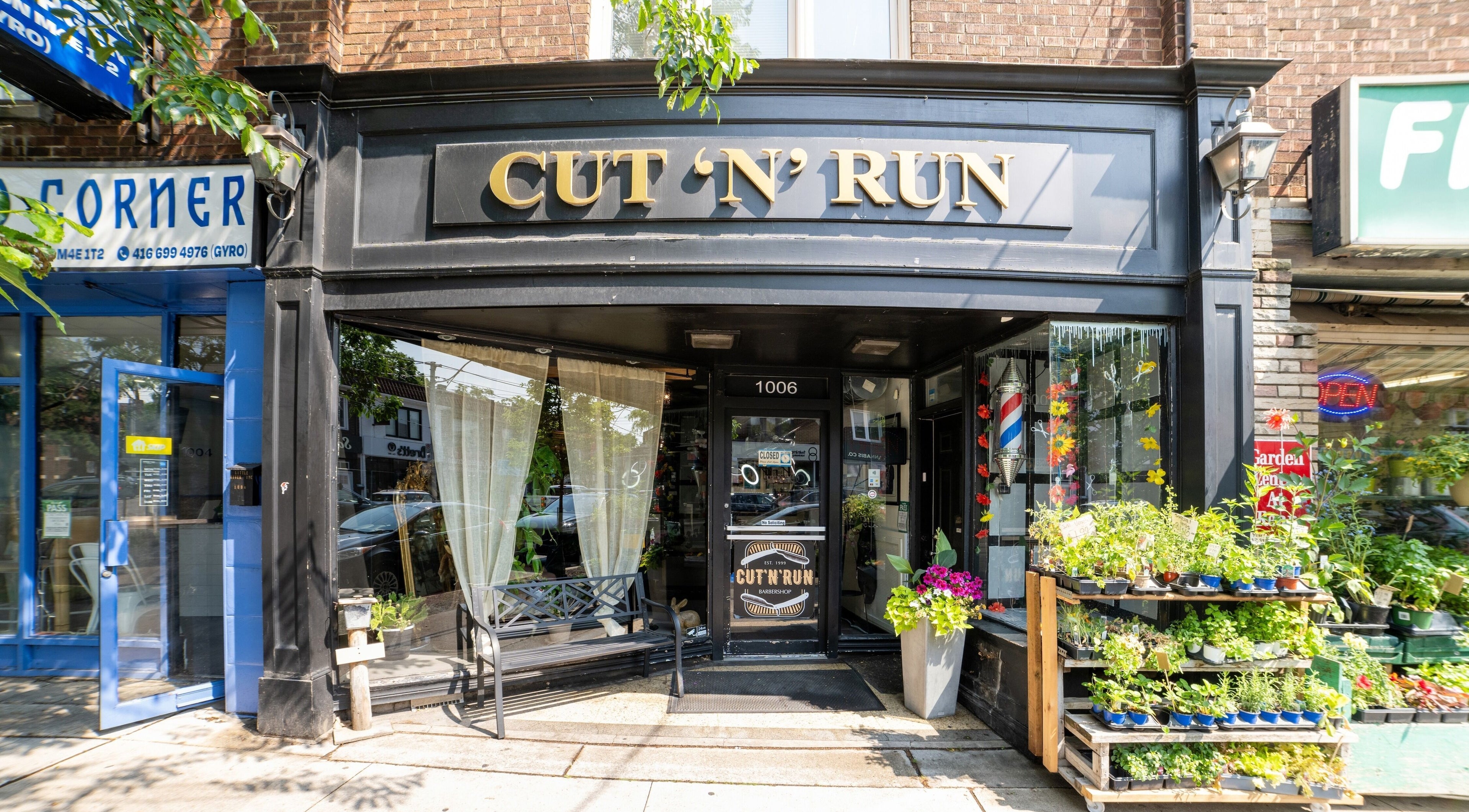 Front view of Cut N Run Barbershop in Toronto, Ontario, CA, with its stylish black facade and lush greenery.