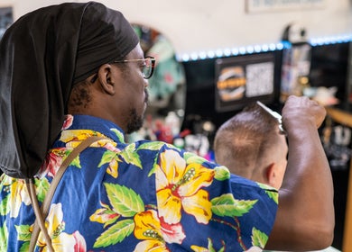Barber in floral shirt cutting hair at Cut N Run Barbershop, Toronto, Ontario, CA.