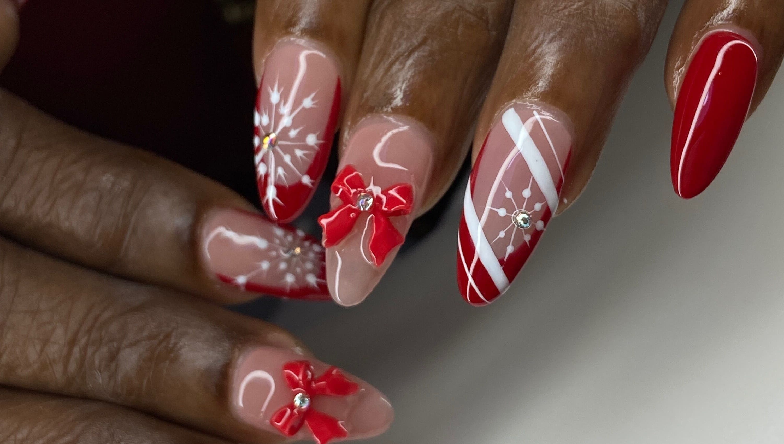Red and white festive nail art at Kshine Aesthetics, Brievengat, Curaçao, CW. Intricate bows and snowflake designs.