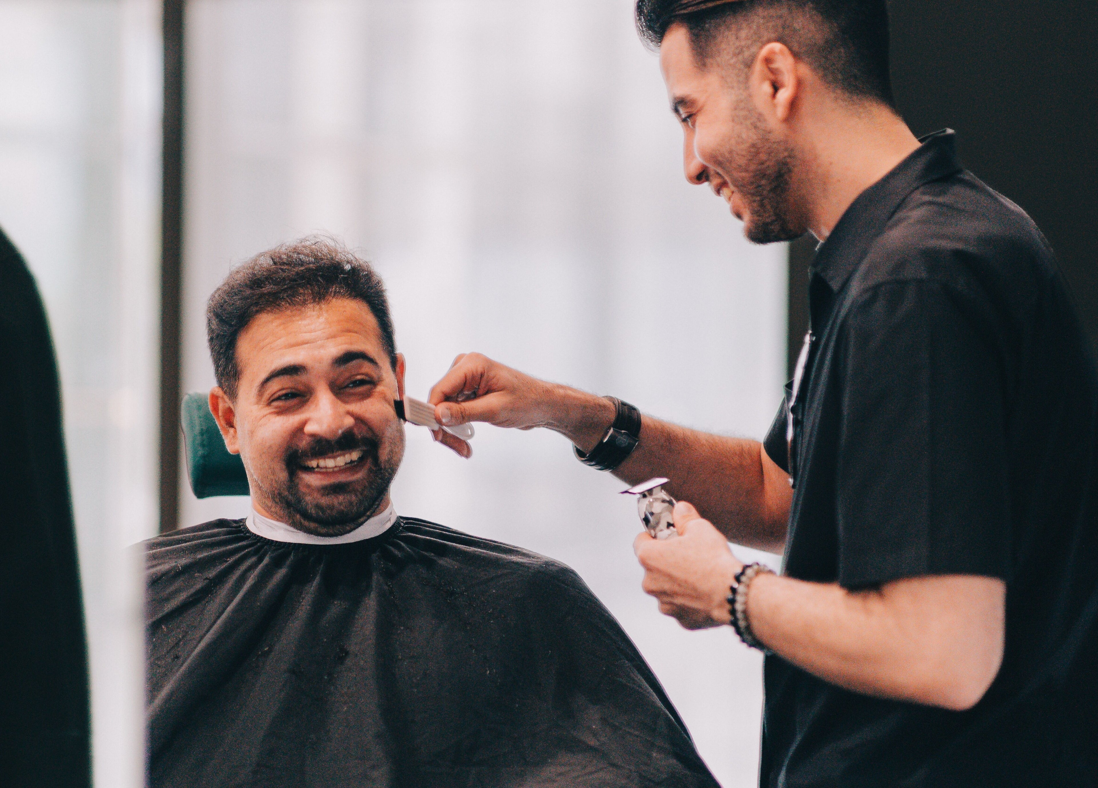 A barber at BarberBar at Pavilion Embassy smiles while trimming a client's beard in Kuala Lumpur, Wilayah Persekutuan Kuala Lumpur, MY.