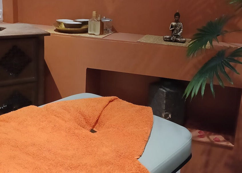 Table de massage sereine à Les Pin Up Au Spa, Marigot, MF, décorée avec une couverture orange et une statue zen.