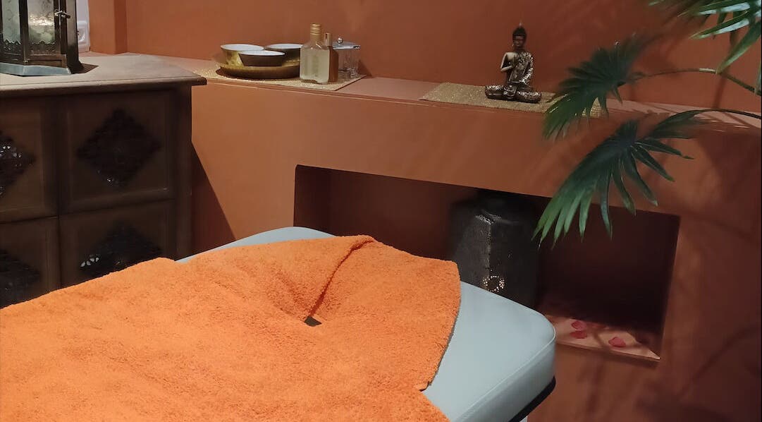 Table de massage sereine à Les Pin Up Au Spa, Marigot, MF, décorée avec une couverture orange et une statue zen.