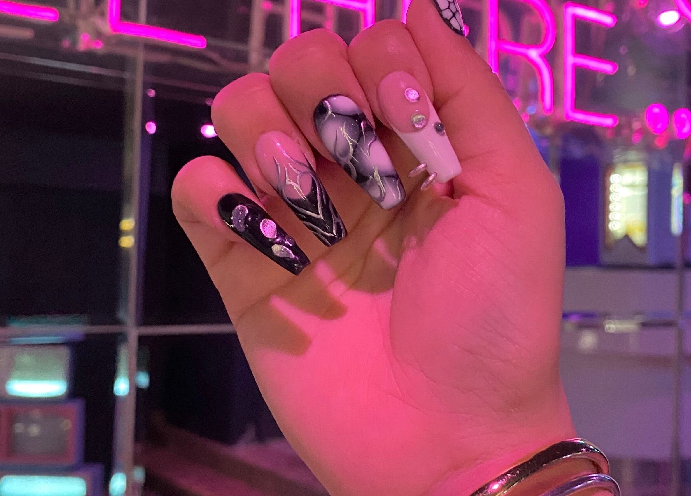 Uñas acrílicas artísticas en Meloody Nails, Cali, Valle Del Cauca, CO, con luces de neón de fondo.
