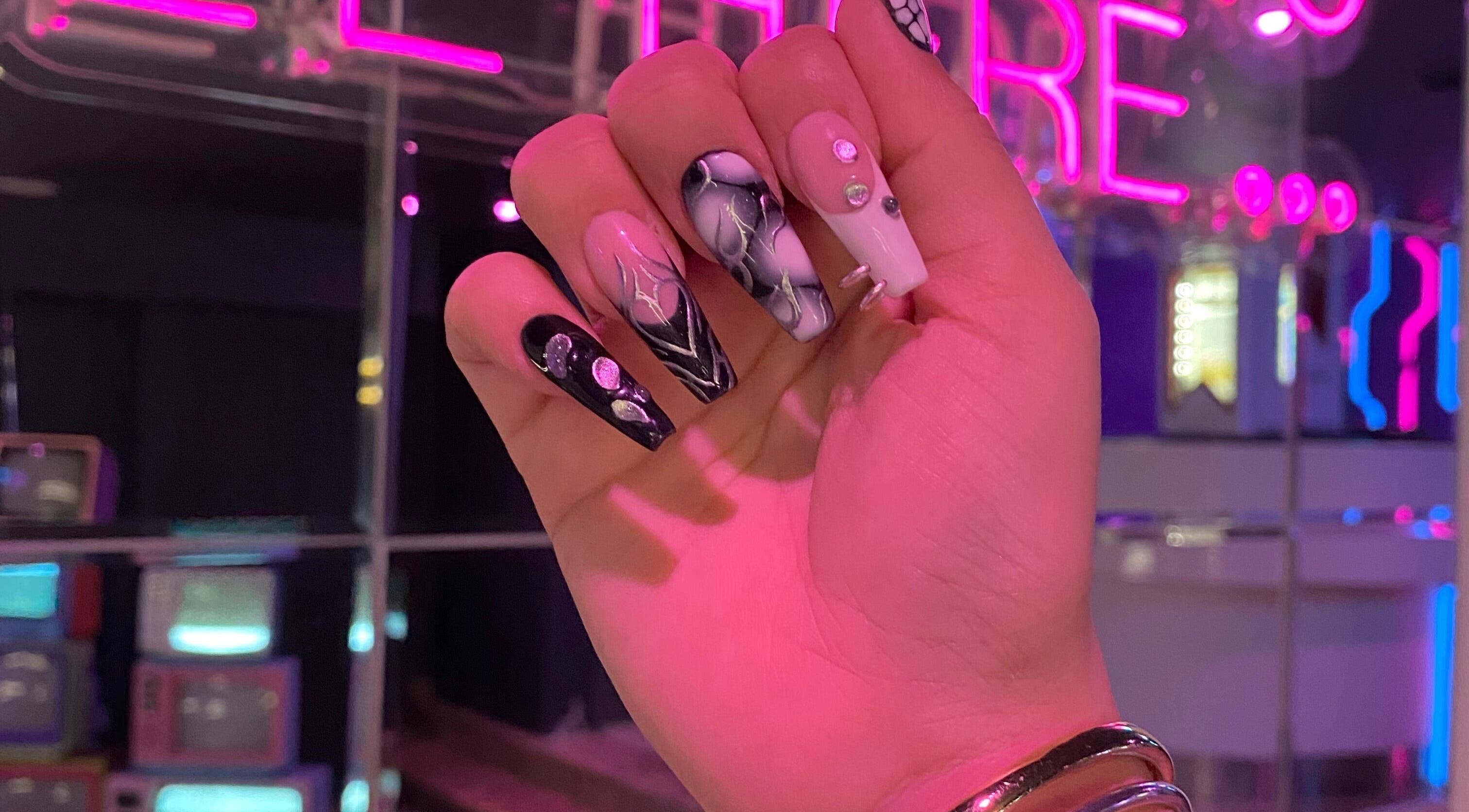Uñas acrílicas artísticas en Meloody Nails, Cali, Valle Del Cauca, CO, con luces de neón de fondo.