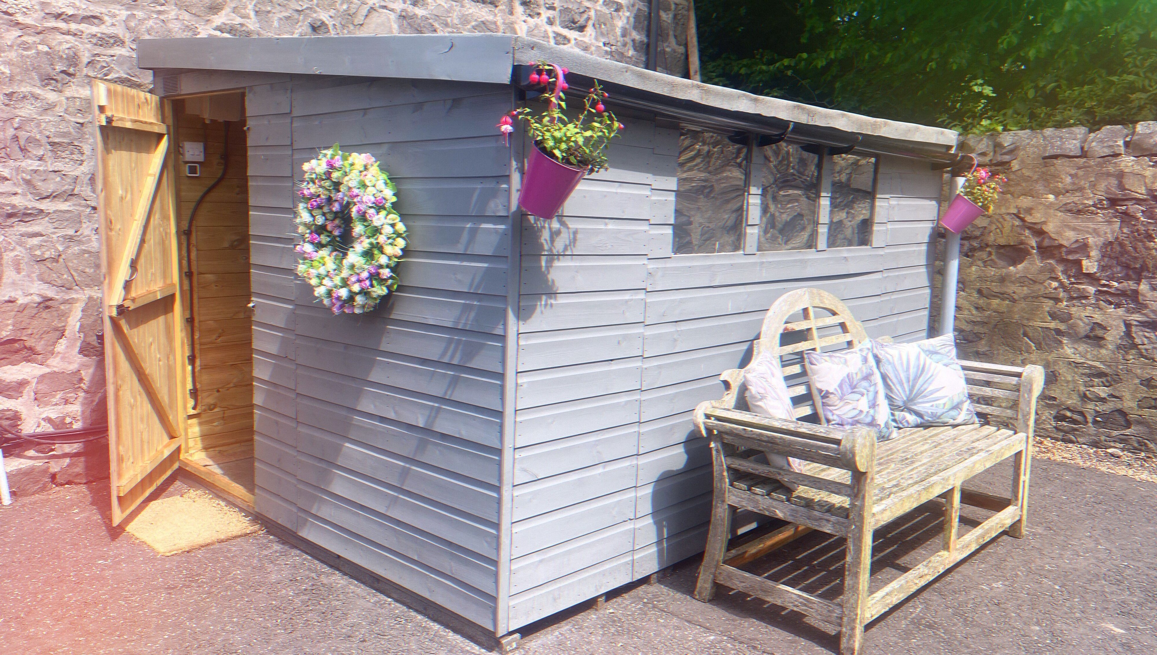 Charming shed entrance at GLOW Spray Tanning by Rachel, Dundee, GB, with floral wreath and bench.