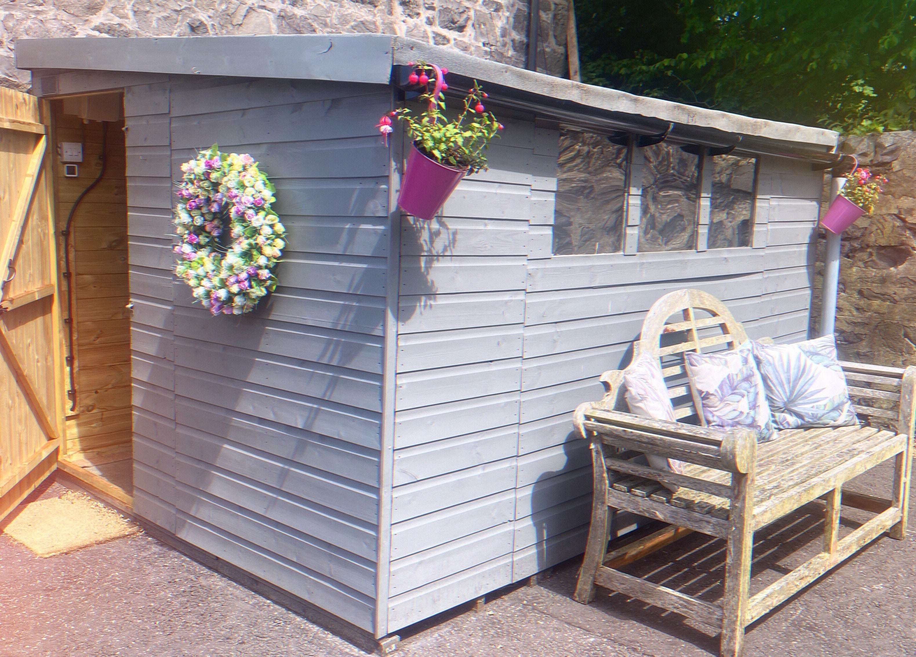Charming shed entrance at GLOW Spray Tanning by Rachel, Dundee, GB, with floral wreath and bench.