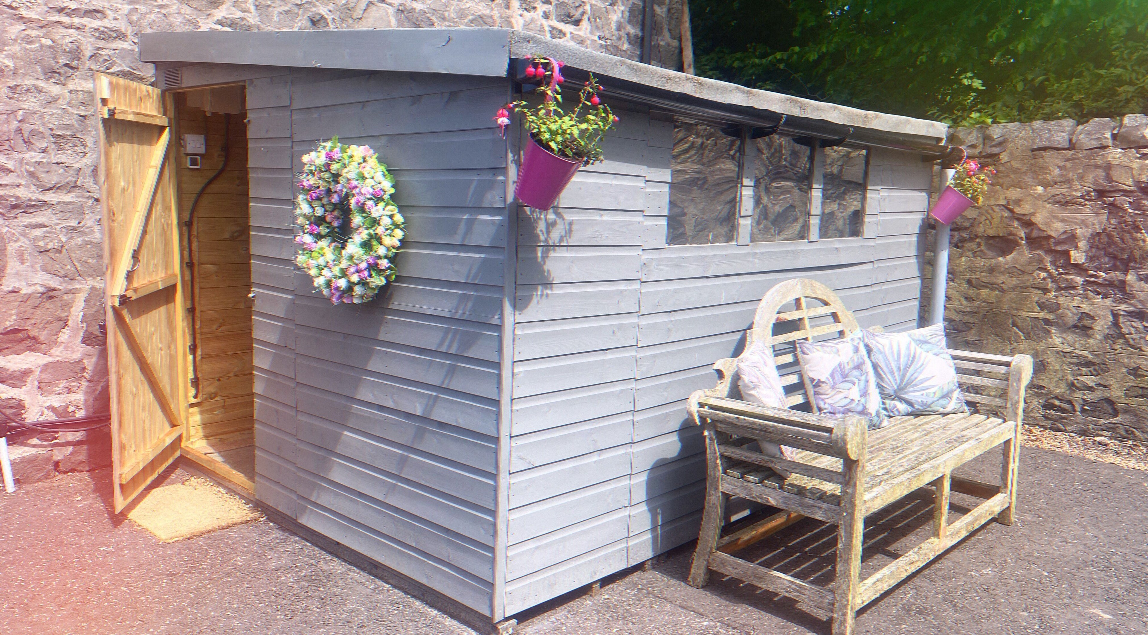 Charming shed entrance at GLOW Spray Tanning by Rachel, Dundee, GB, with floral wreath and bench.