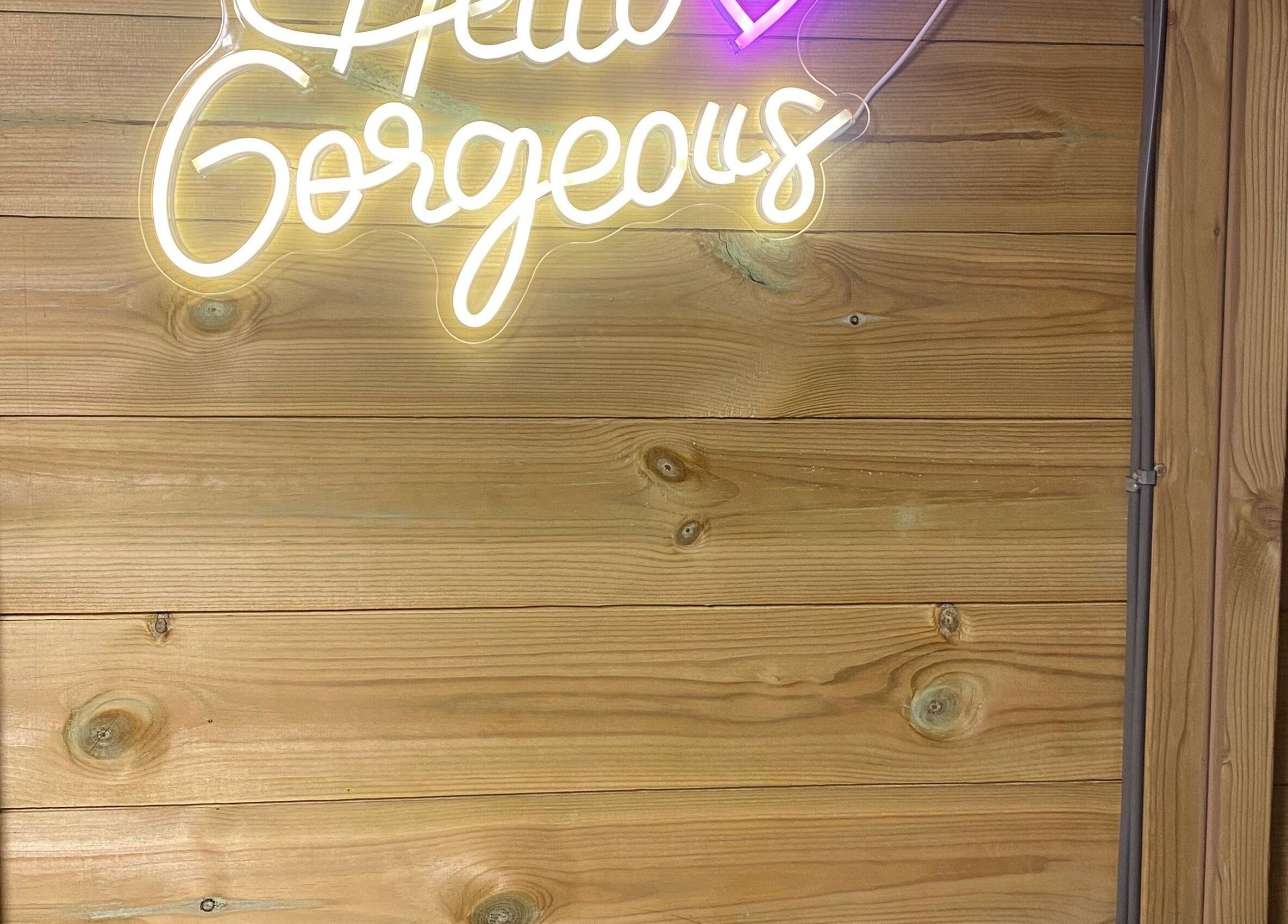 Neon sign 'Hello Gorgeous' at GLOW Spray Tanning by Rachel in Dundee, GB on a wooden wall.