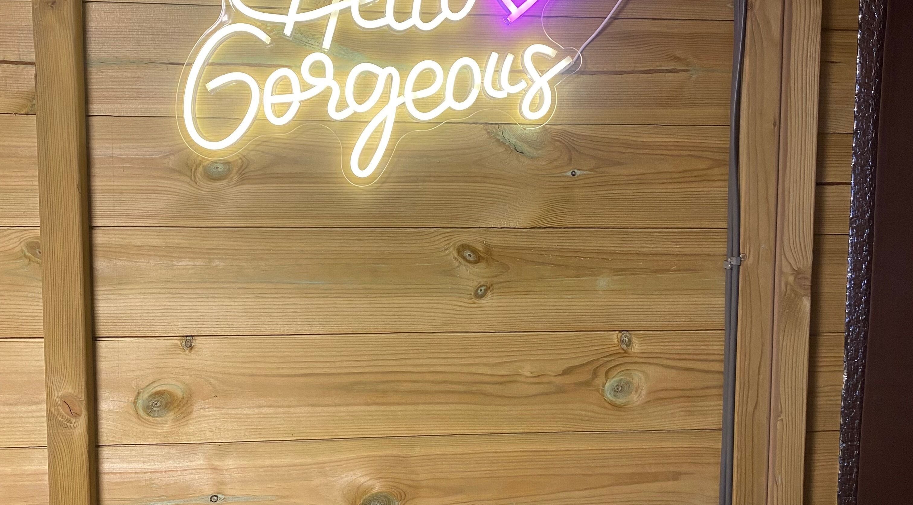Neon sign 'Hello Gorgeous' at GLOW Spray Tanning by Rachel in Dundee, GB on a wooden wall.