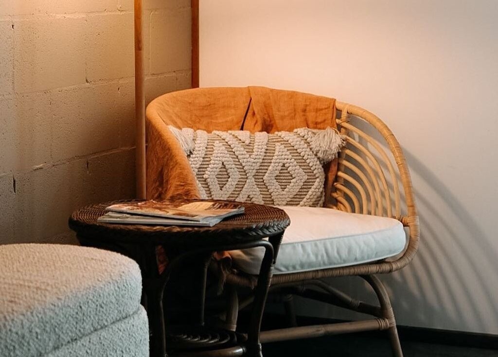 Cozy seating area at Feather and Arch Cosmetic Tattoo, Mooloolaba, Queensland, AU with rattan chair and cushions.