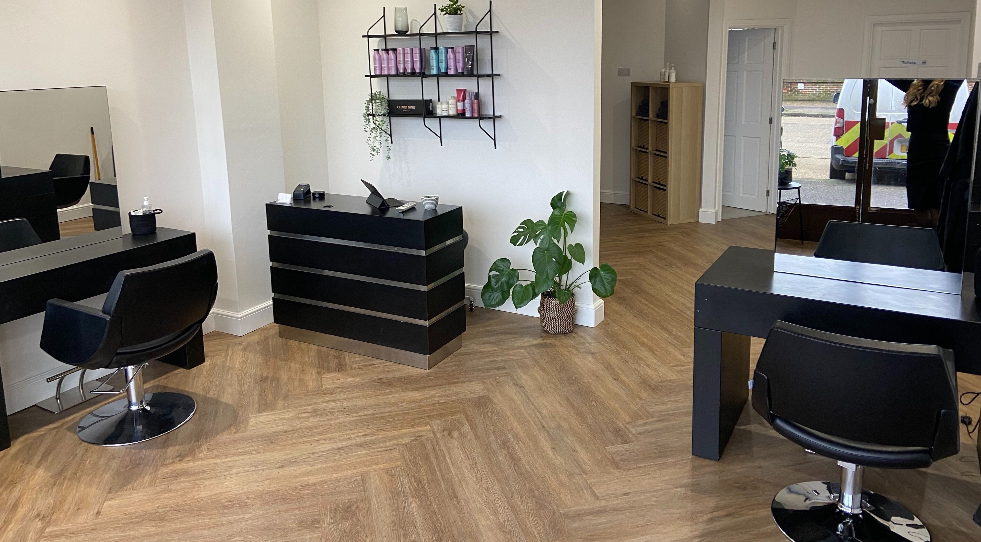 Modern interior of Melanie Payne Hair Studio in Goring-by-Sea, England, showcasing sleek black chairs and wooden flooring.