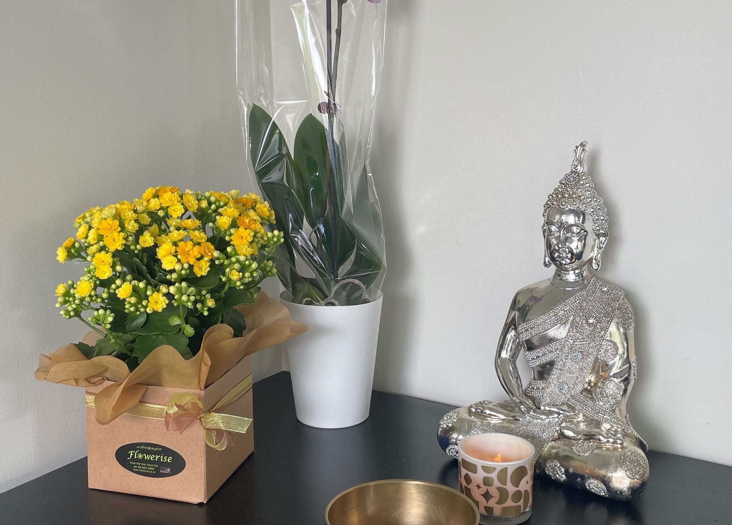 Peaceful setup at Meena’s Beauty & Skincare, Auckland, with flowers, a candle, and a silver Buddha statue.