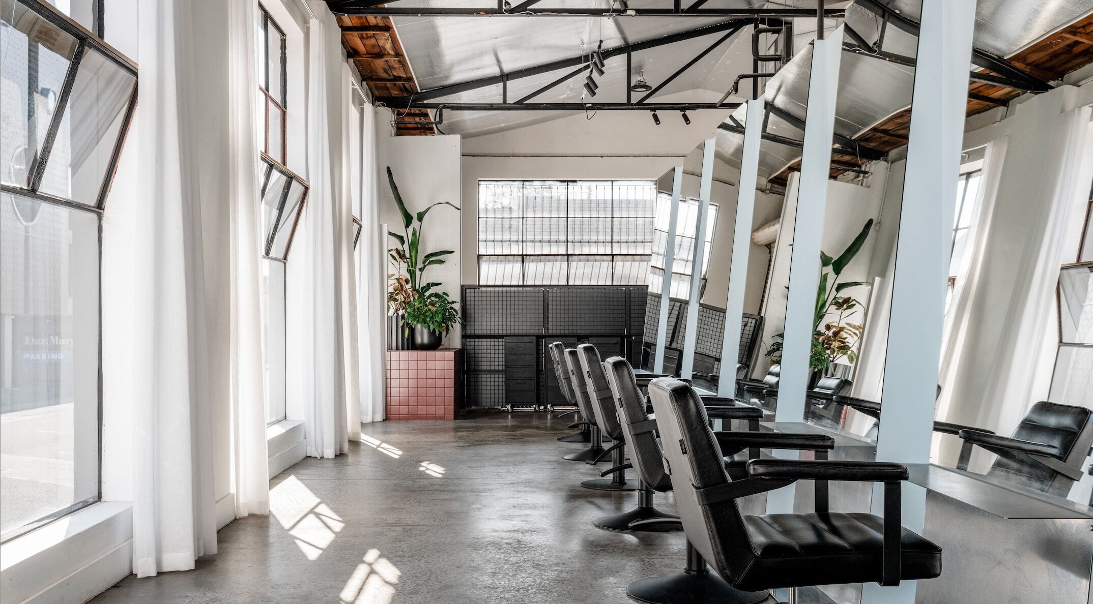 Light-filled interior of Alchemy Salon in Melbourne, Victoria, AU with sleek black salon chairs and mirrors.