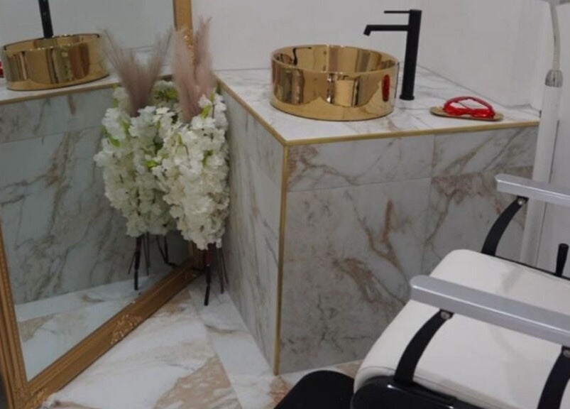 Luxurious vanity area at Athena Mortlake, London, England, GB with gold sink and marble tiles.