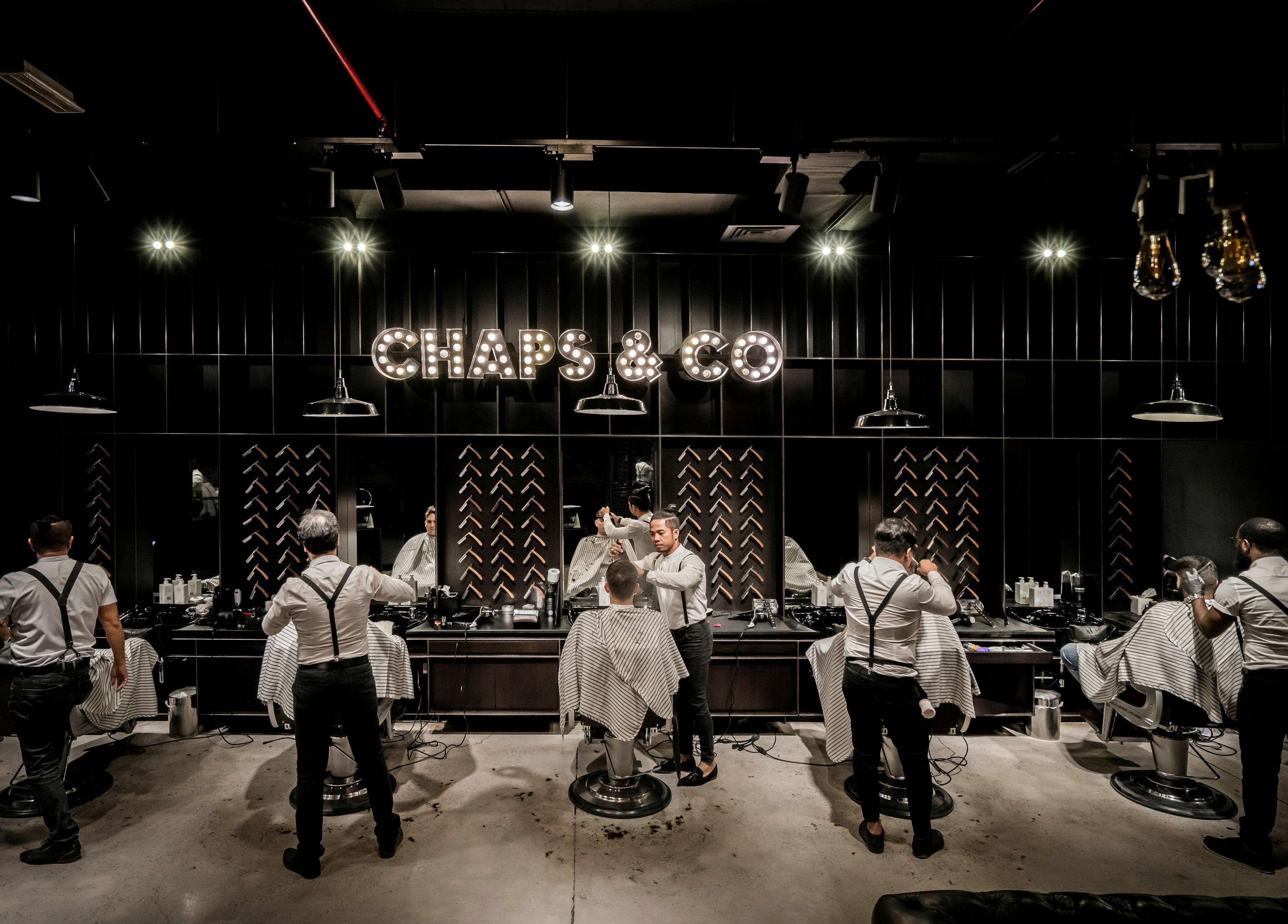 Interior of Chaps & Co - JLT barbershop in Dubai, AE with stylists attending clients in a dimly lit setting.