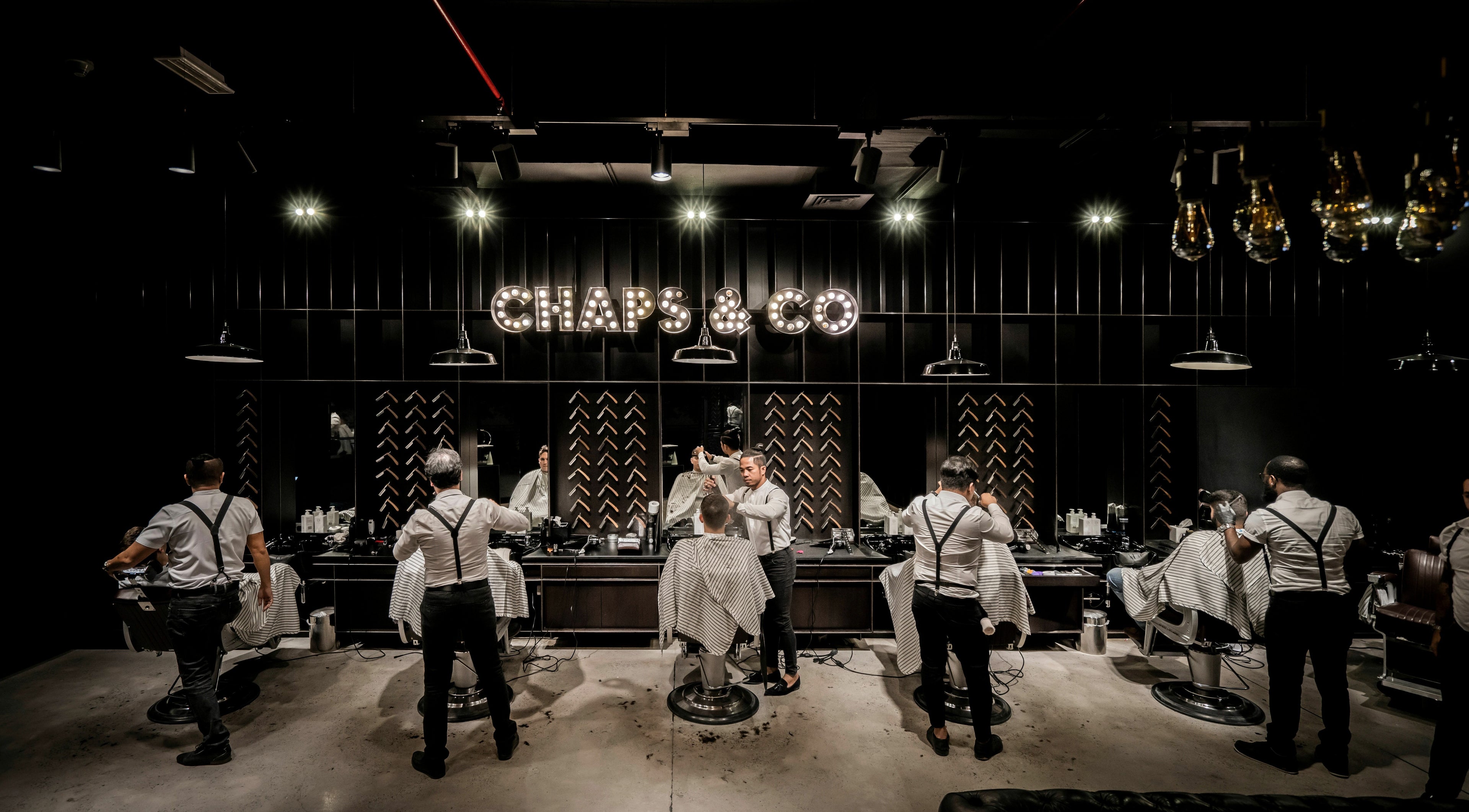 Interior of Chaps & Co - JLT barbershop in Dubai, AE with stylists attending clients in a dimly lit setting.