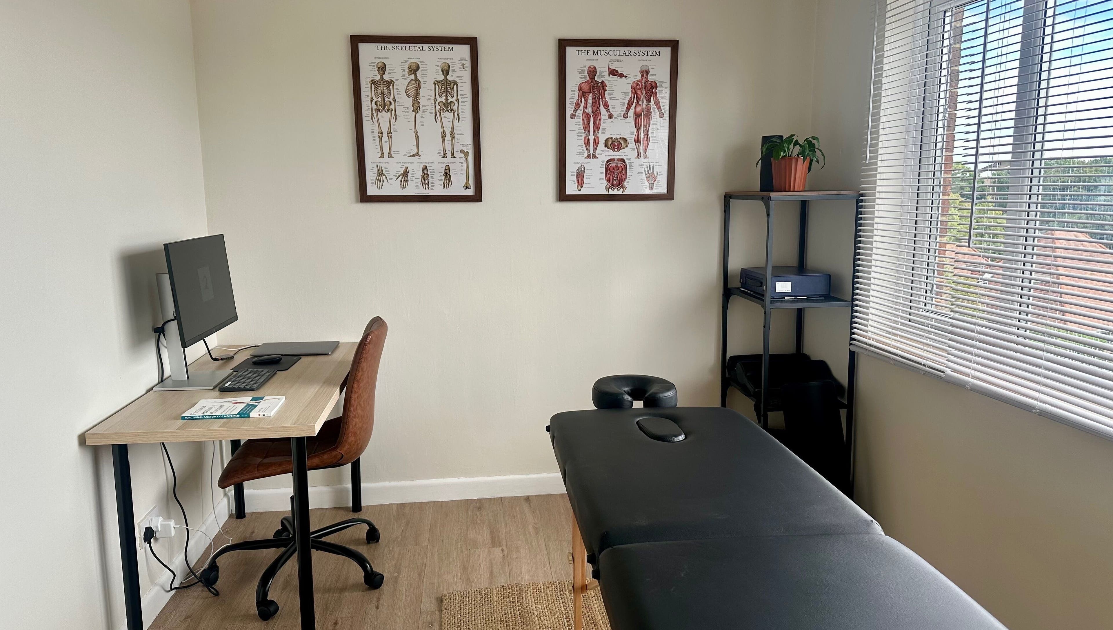 Calm therapy room at Resolve Massage, Bournemouth, England, GB with desk, massage table, and anatomical charts.