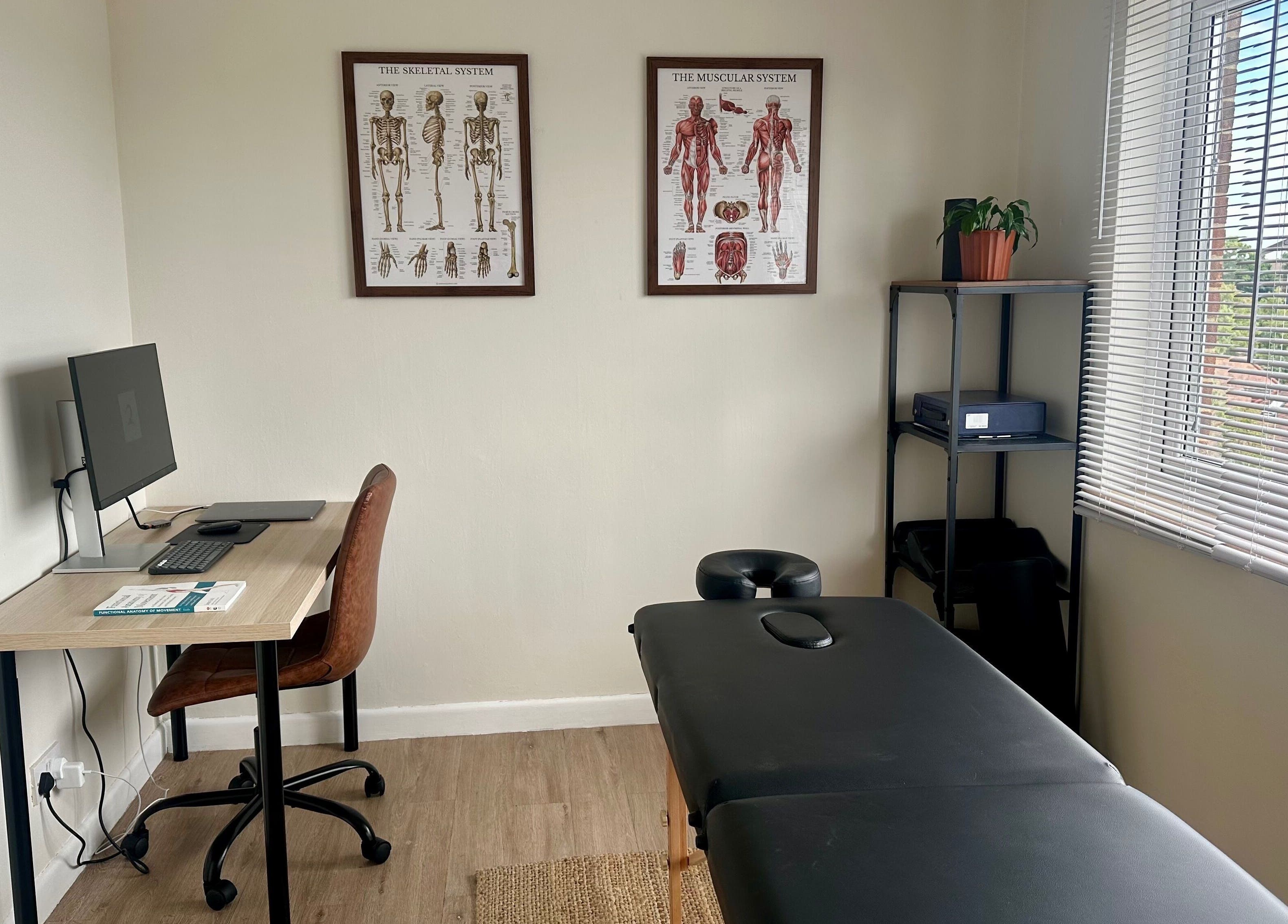 Calm therapy room at Resolve Massage, Bournemouth, England, GB with desk, massage table, and anatomical charts.