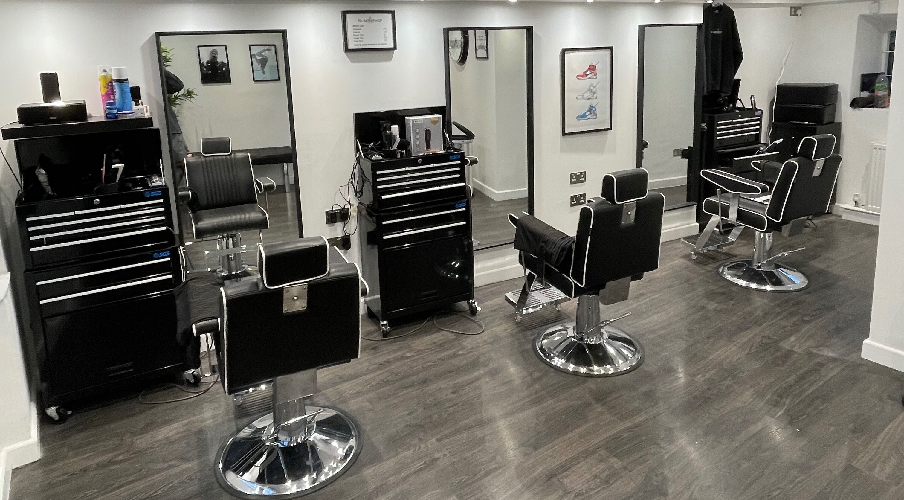 Stylish interior of TQs Barbershop in Malmesbury, England, featuring sleek black barber chairs and mirrors.