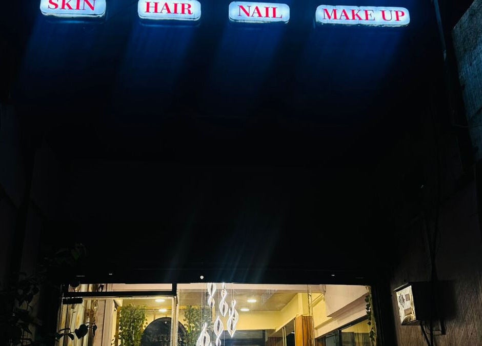 Entrance of Naturā Unisex Salon in Pune, Maharashtra, IN, with glowing signs for skin, hair, nail, and make up services.