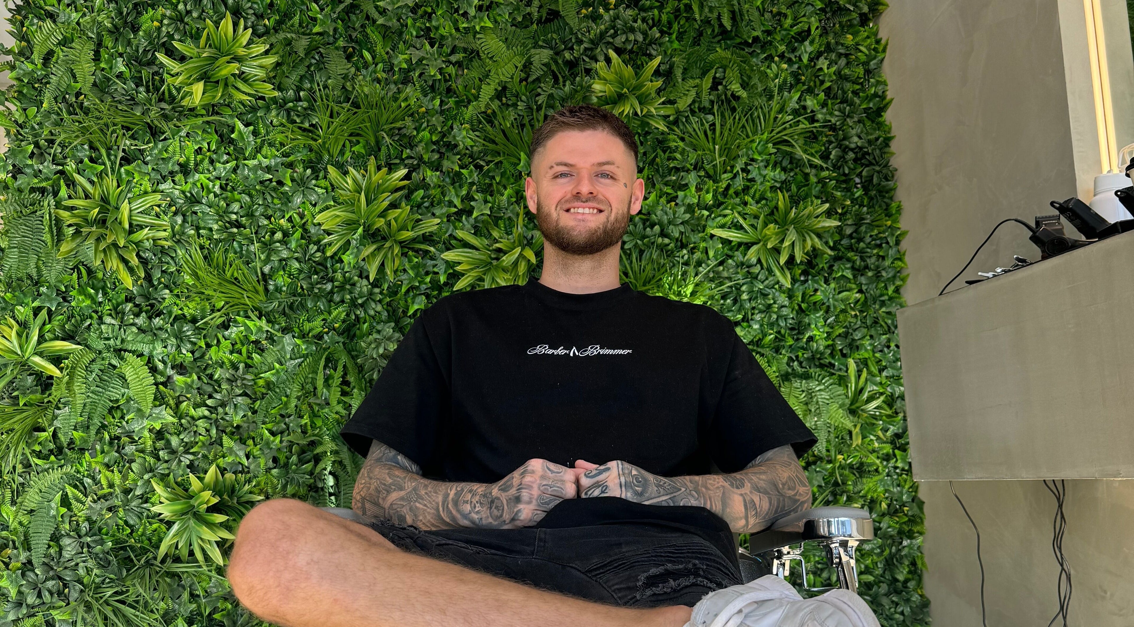Barber in chair at Barber Brimmer, lush green wall, Melbourne, Victoria, AU.