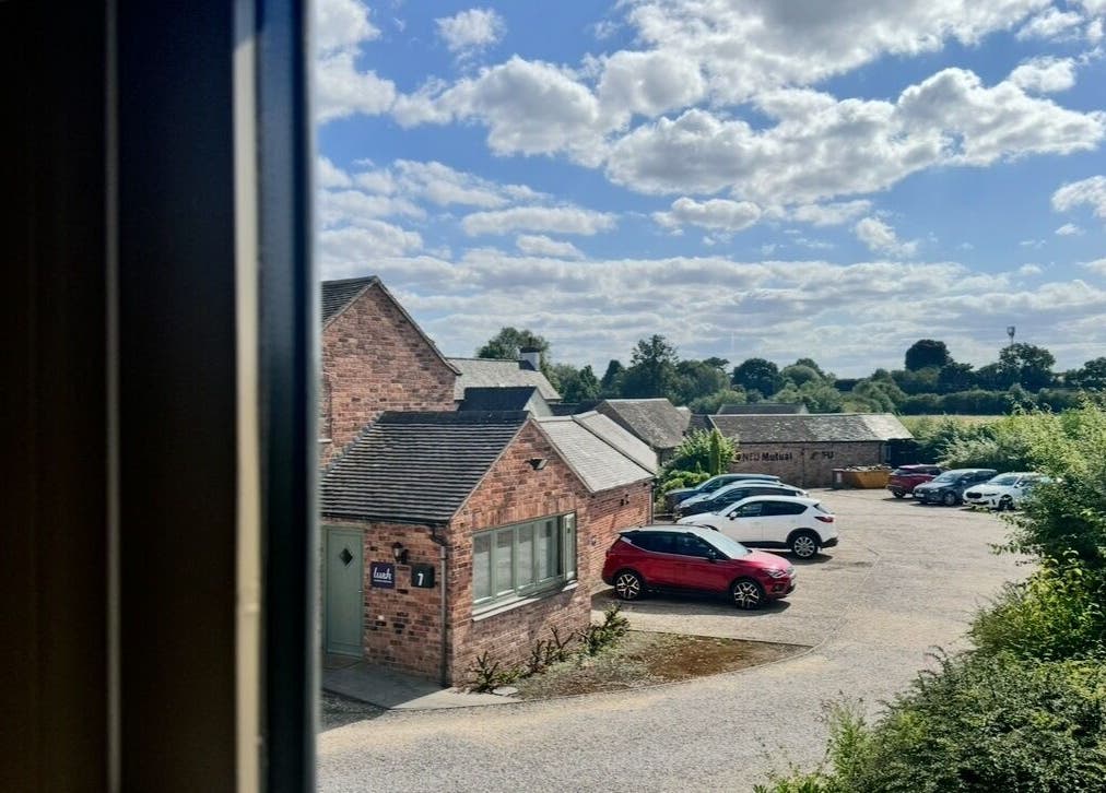 View from KK Clinic in Ashby-de-la-Zouch, England featuring rustic brick buildings, greenery, and clear skies.