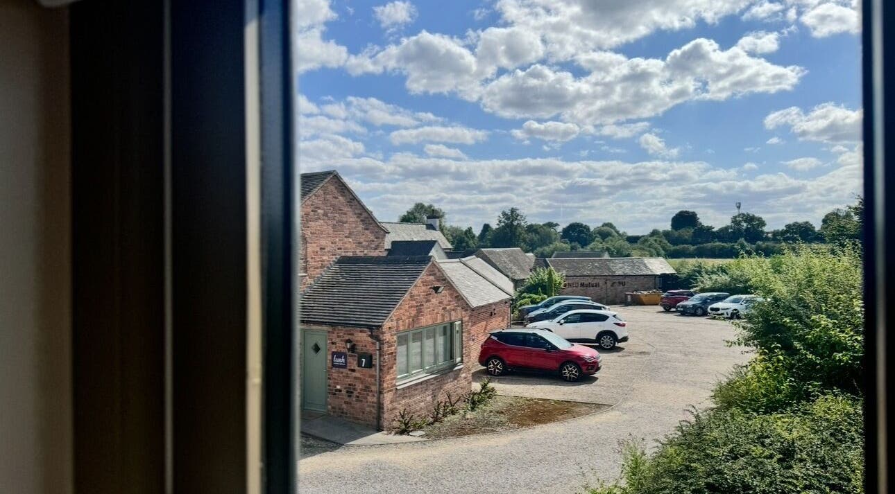 View from KK Clinic in Ashby-de-la-Zouch, England featuring rustic brick buildings, greenery, and clear skies.