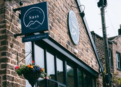 The Sanctuary at Sass entrance with rustic brick facade in Marsden, England, GB, adorned with vibrant hanging flowers.