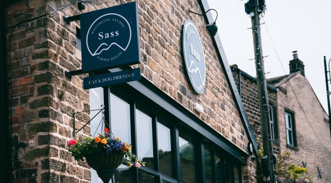 The Sanctuary at Sass entrance with rustic brick facade in Marsden, England, GB, adorned with vibrant hanging flowers.