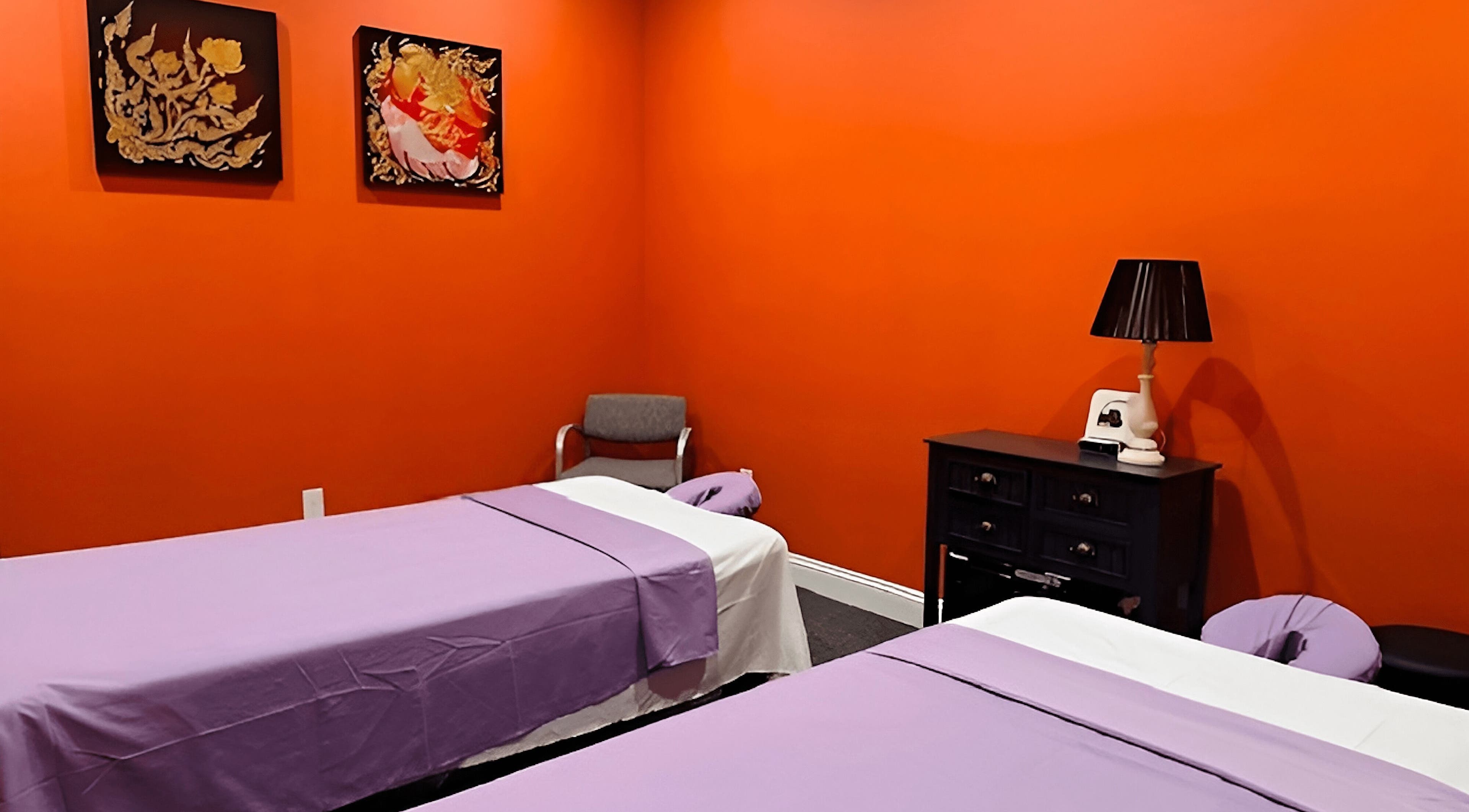 Two massage tables at Erawan@Prosper in Prosper, Texas, US, set in a vibrant orange room with artistic decor.