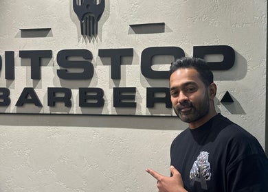 Pitstop Barbers signage in Dubai, AE with a man smiling beside it.