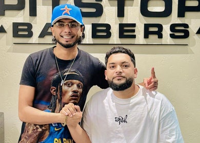 Two men smiling at Pitstop Barbers in Dubai, AE with the shop name visible in the background.