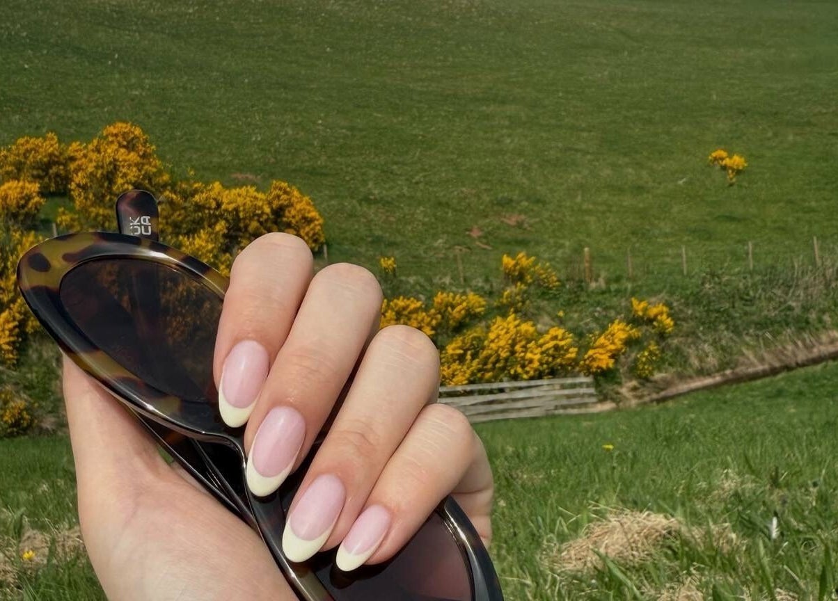 Elegant manicured nails at The Nail Project by Deanna, Penicuik, Scotland, set against a lush green landscape.