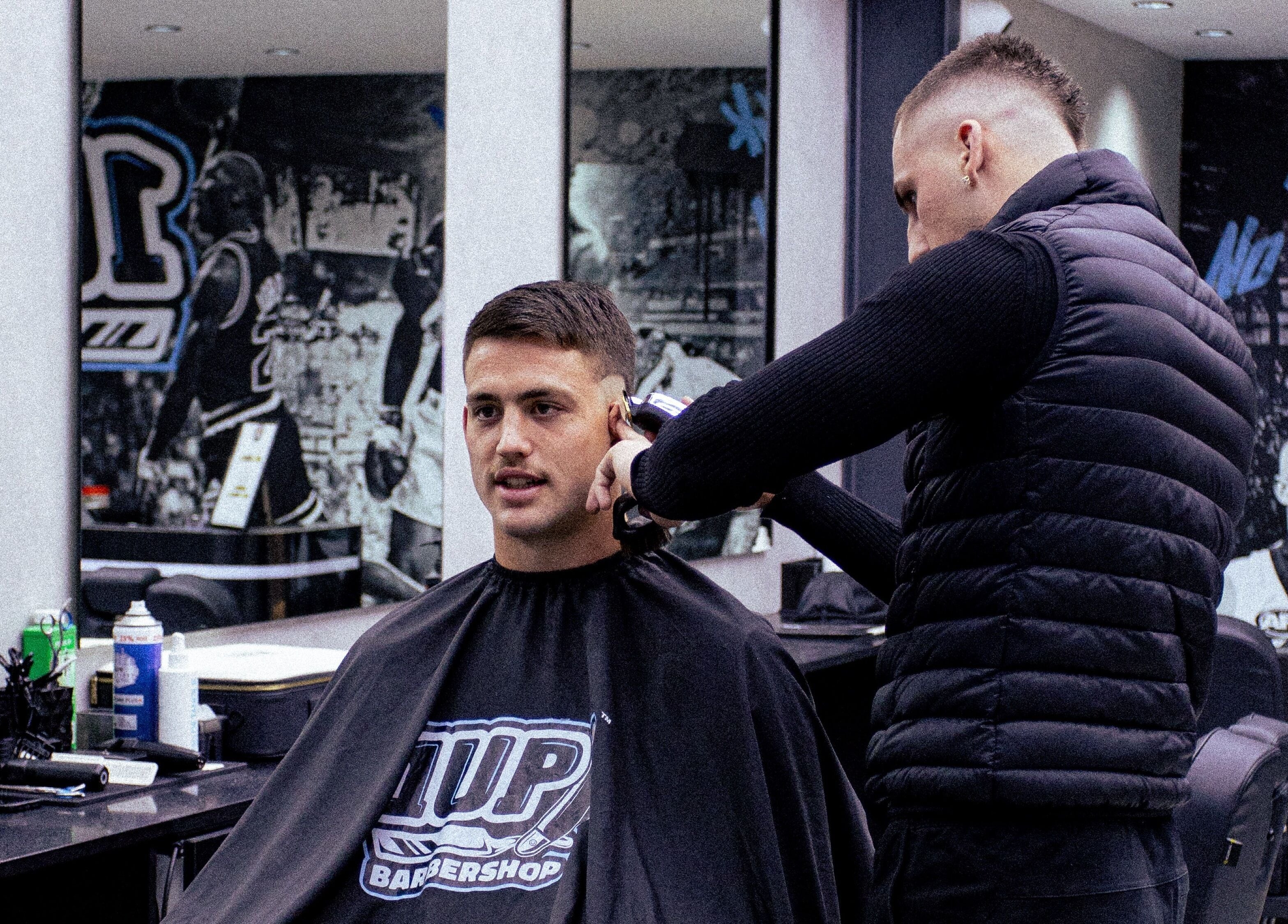 Stylist giving haircut at 1UP Barbershop Bicton in Bicton, Western Australia, AU with vibrant interior art.