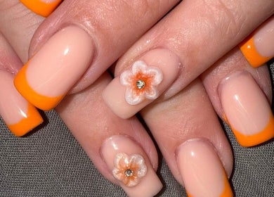 Elegant nail art with orange French tips and flower design at The Luxury Nail Bar, Tweedbank, Scotland, GB.